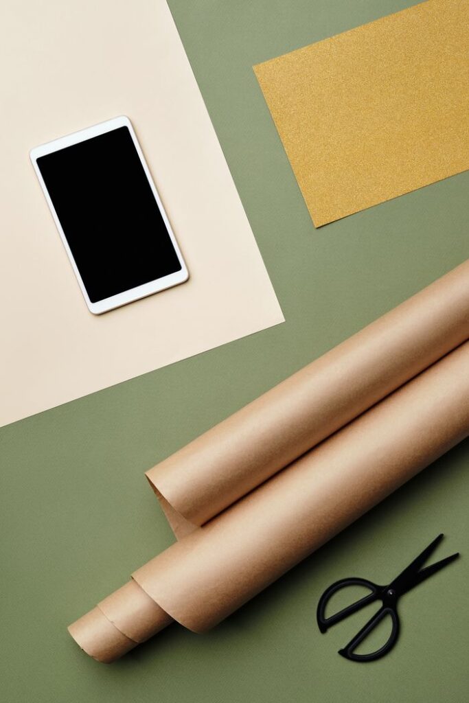 Artistic flat lay of craft supplies, including paper rolls, a smartphone, and scissors on a colorful background.